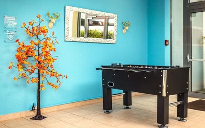 A recreational area featuring a black foosball table against a bright turquoise wall, decorative artwork, a mirror and tiled flooring at Best Western Macrander Hotel Frankfurt/Kaiserlei.