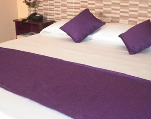 White bed with purple cushions and a matching bed runner against a patterned headboard at Caribe Panamá Hotel.