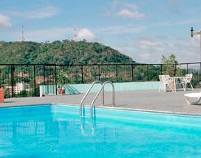 Rooftop swimming pool with white loungers, black railings and a green hillside in the background at Caribe Panamá Hotel.