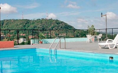 Rooftop swimming pool with white loungers, black railings and a green hillside in the background at Caribe Panamá Hotel.