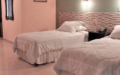 Two single beds with white bedding, a patterned headboard wall and dark curtains at Caribe Panamá Hotel.