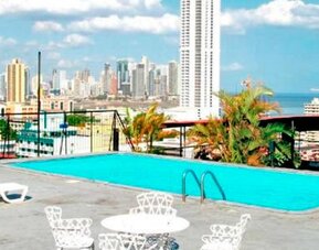 Rooftop swimming pool with white loungers and views of Panama City's skyline and ocean at Caribe Panamá Hotel.