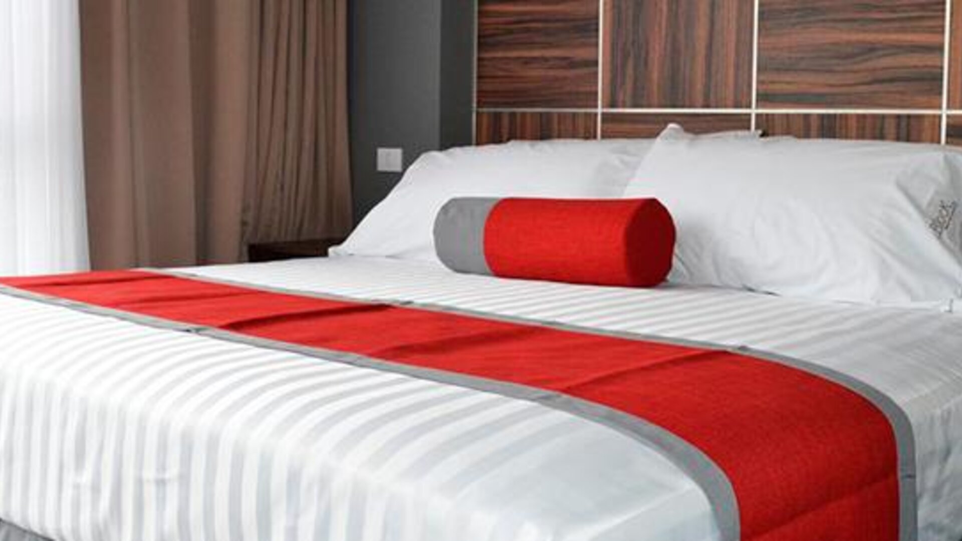 King-size bed with white striped bedding, red runner and cylindrical accent cushion against a dark wood-panelled headboard at Hotel Block Suites.