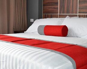 King-size bed with white striped bedding, red runner and cylindrical accent cushion against a dark wood-panelled headboard at Hotel Block Suites.