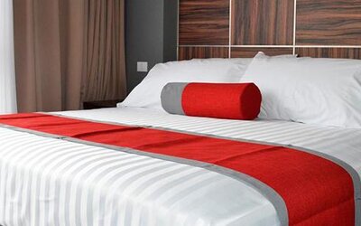 King-size bed with white striped bedding, red runner and cylindrical accent cushion against a dark wood-panelled headboard at Hotel Block Suites.