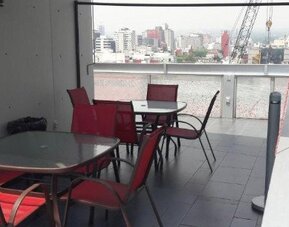 Outdoor terrace with tables and red chairs, glass railing and elevated views of the surrounding city at Hotel Block Suites.