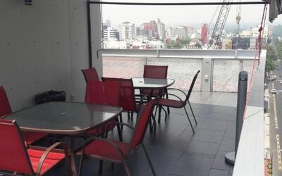 Outdoor terrace with tables and red chairs, glass railing and elevated views of the surrounding city at Hotel Block Suites.