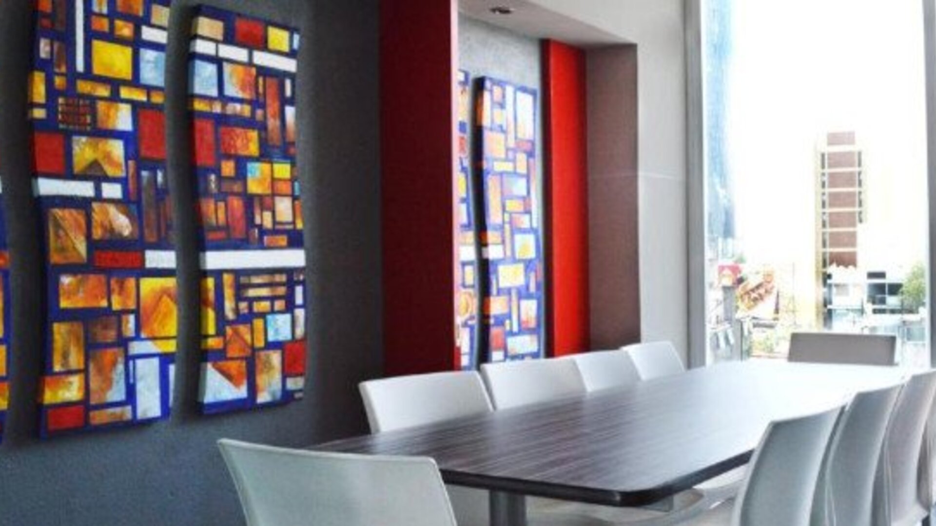 Meeting room with a long conference table, white chairs, colourful geometric wall art and large windows overlooking the city at Hotel Block Suites.