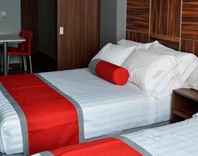 Twin beds with white striped bedding, red runners and cylindrical cushions, dark wood headboard and a small dining table at Hotel Block Suites.