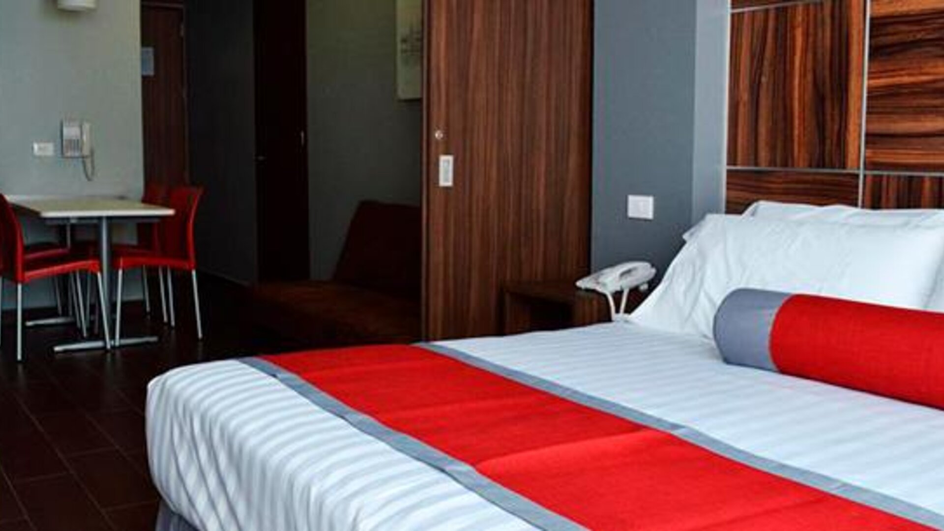 King-size bed with white bedding, red accent runner and cushion, wood-panelled headboard and bedside telephone at Hotel Block Suites.