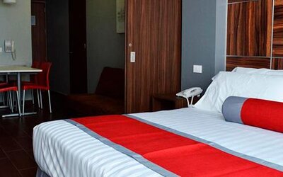 King-size bed with white bedding, red accent runner and cushion, wood-panelled headboard and bedside telephone at Hotel Block Suites.