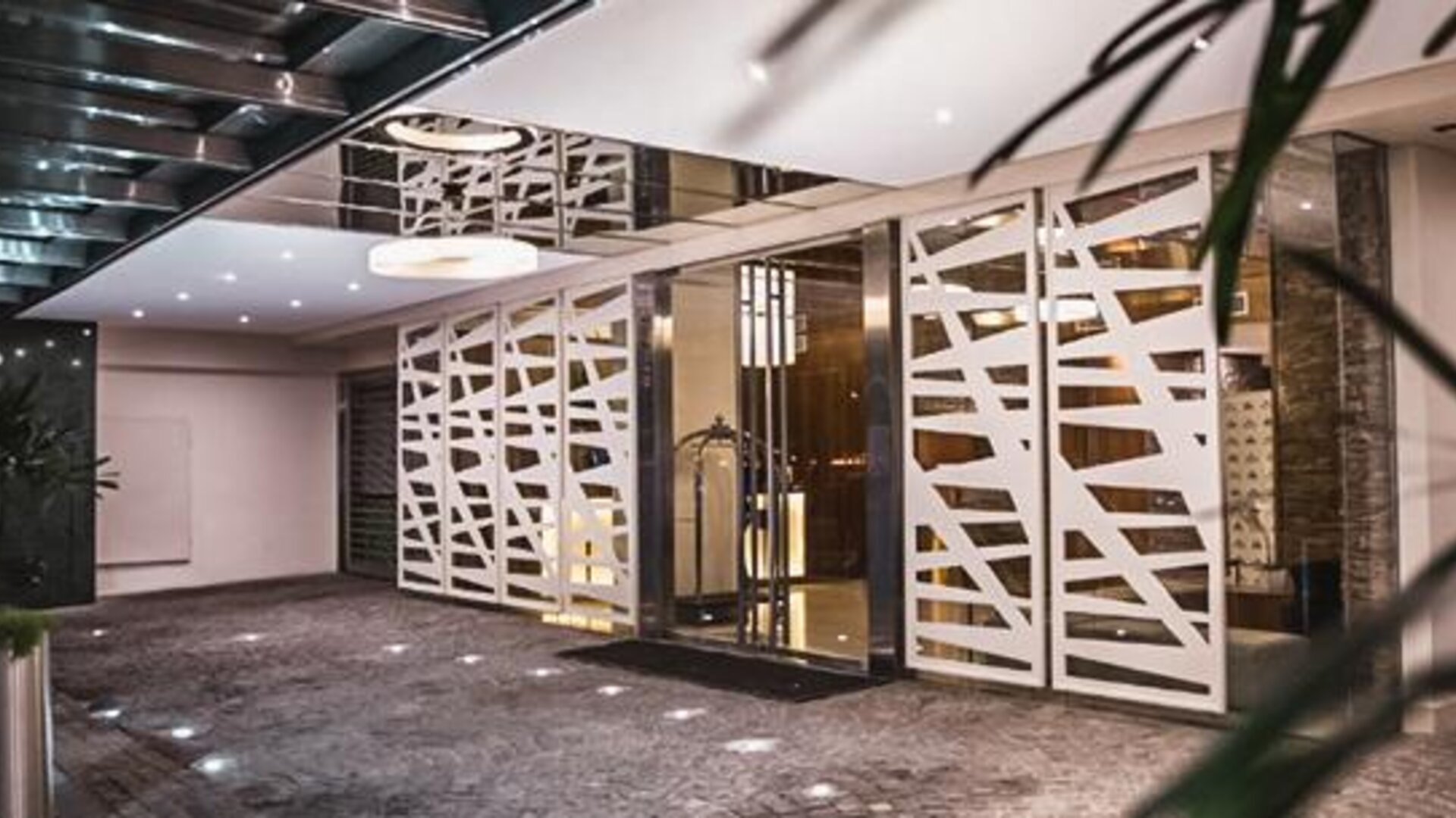 Hotel entrance with glass doors, white geometric screens, dark stone flooring and potted plants at Howard Johnson Plaza Buenos Aires.
