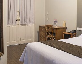Guest room with a bed beside a wooden desk and chair, with a large wall mirror at Hotel Principal.