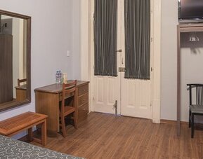 Work area with a wooden desk, chair, wall-mounted television and large mirror at Hotel Principal.
