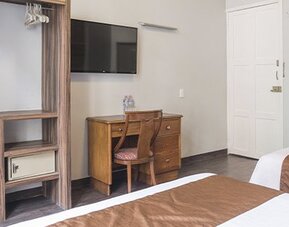 Guest room workspace with a wooden desk, chair and television mounted above the desk at Hotel Principal.