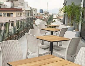 Outdoor terrace dining area with wooden tables, white woven chairs and city views at Hotel Principal.