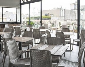 Indoor dining area with square tables, grey woven chairs and floor-to-ceiling windows at Hotel Principal.