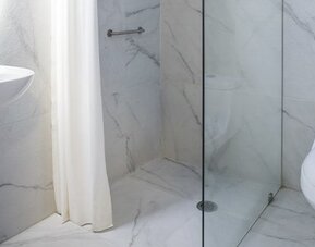 Bathroom with white marble-effect tiles, pedestal sink, glass-enclosed shower and toilet at Hotel Principal.