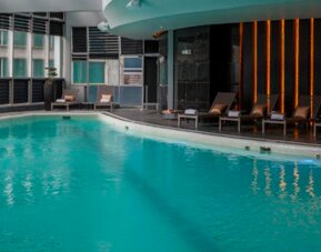 Indoor swimming pool with turquoise water, loungers and floor-to-ceiling windows at Hotel Las Américas Golden Tower Panamá.