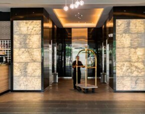 Hotel lobby entrance with illuminated stone columns, polished flooring and a luggage trolley at Hotel Las Américas Golden Tower Panamá.