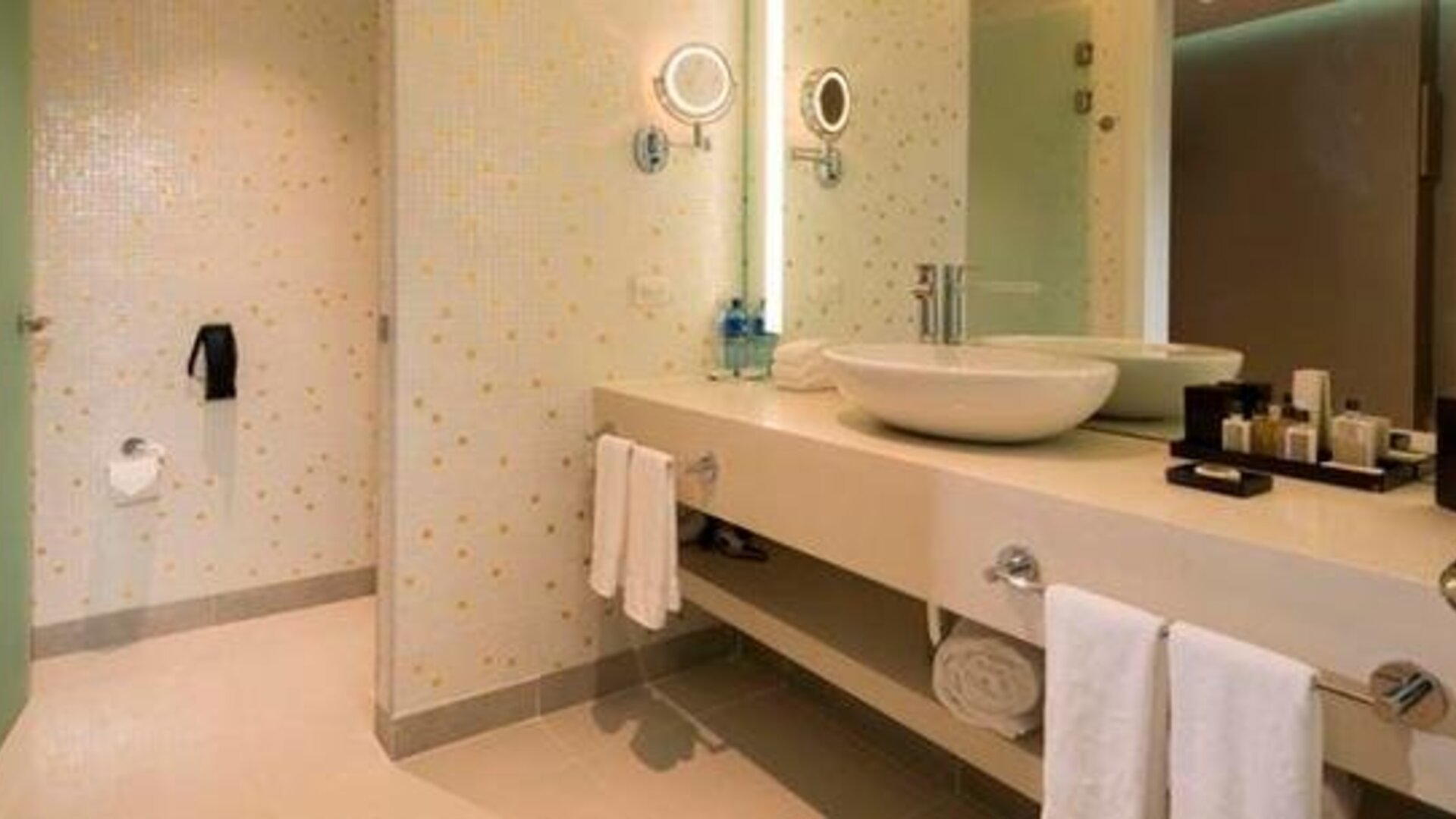Modern bathroom with a walk-in shower, twin vessel sinks, large mirrors and folded towels at Hotel Las Américas Golden Tower Panamá.
