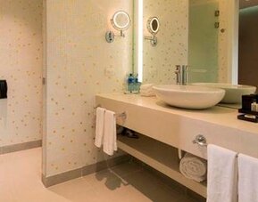 Modern bathroom with a walk-in shower, twin vessel sinks, large mirrors and folded towels at Hotel Las Américas Golden Tower Panamá.