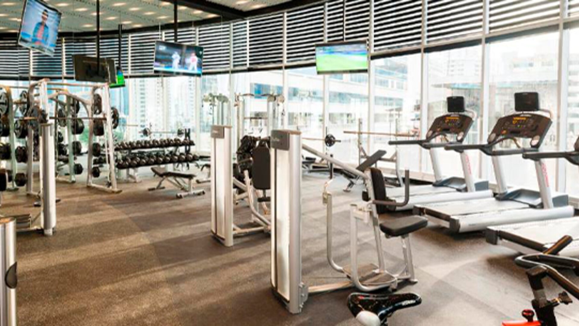 Fitness centre with treadmills, weight machines, dumbbells and large windows overlooking the city at Hotel Las Américas Golden Tower Panamá.