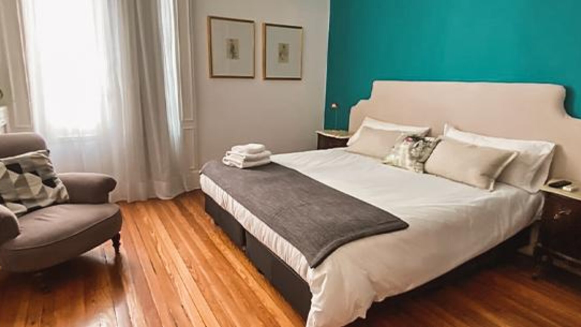 1. Guest bedroom with a king-size bed, teal accent wall, white bedding, grey throw and an armchair beside tall windows at Hotel Chemin.