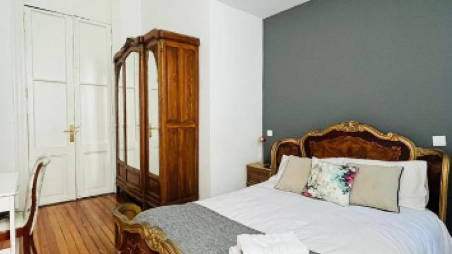 Guest bedroom with an ornate carved wooden bed, white bedding, a grey throw, polished wooden flooring and a wooden wardrobe at Hotel Chemin.