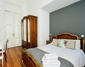 Guest bedroom with an ornate carved wooden bed, white bedding, a grey throw, polished wooden flooring and a wooden wardrobe at Hotel Chemin.