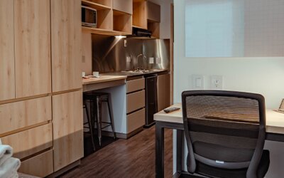 Studio interior with wooden cabinetry, a compact kitchenette, desk, office chair and dark wood-effect flooring at UMA Suites Chía.