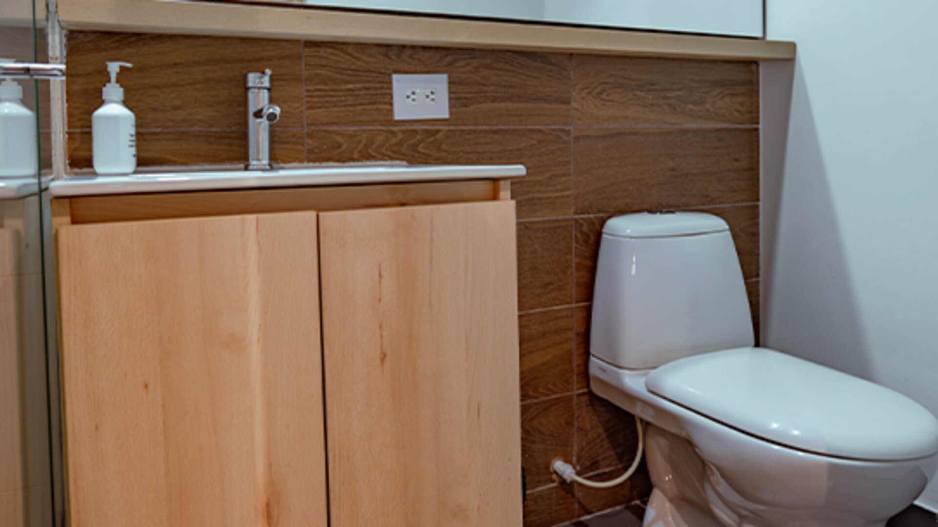 Bathroom with a light wood vanity, white sink, wall-mounted mirror and wood-effect tiled backsplash at UMA Suites Chía.