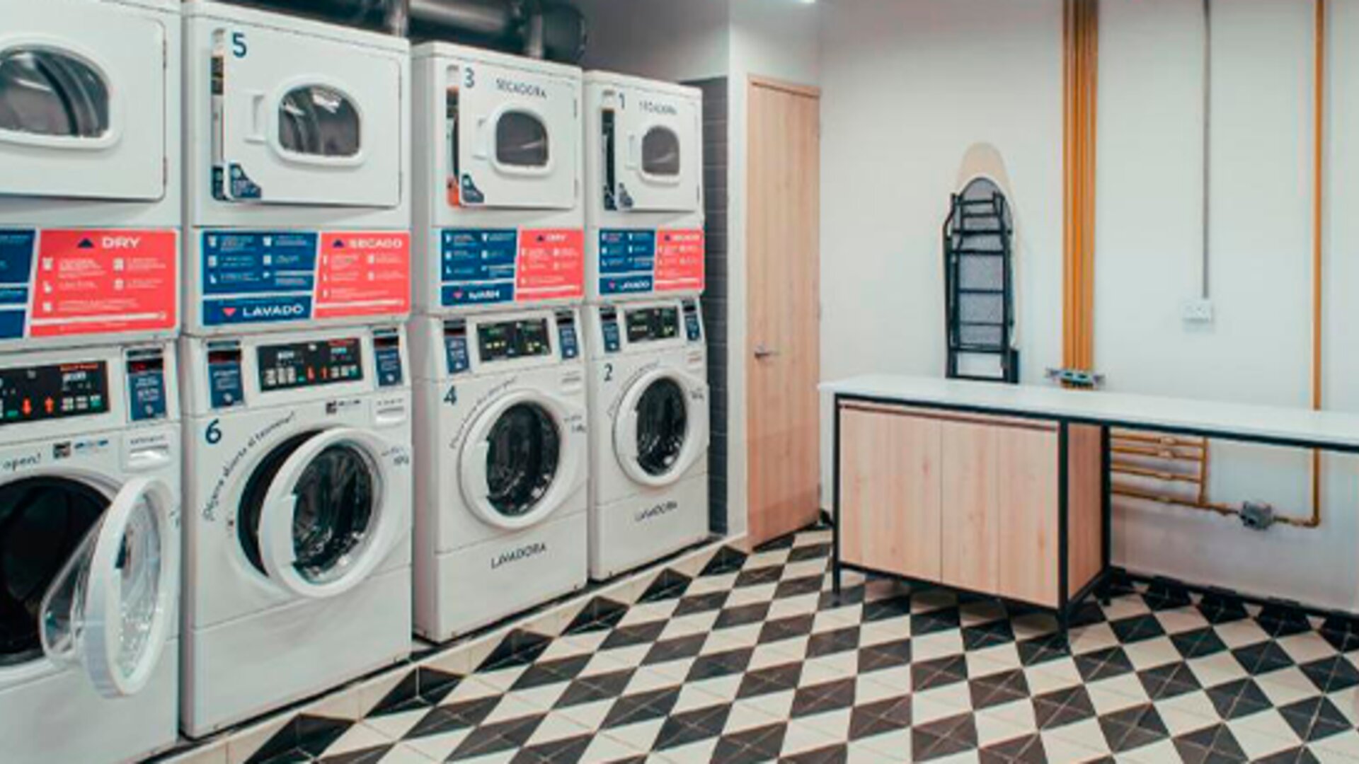Laundry room with rows of stacked washing machines and dryers, folding space and ironing boards at UMA Suites Chía.