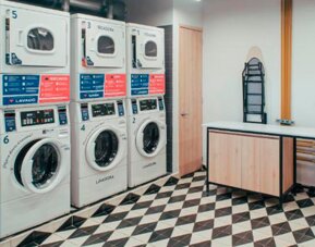 Laundry room with rows of stacked washing machines and dryers, folding space and ironing boards at UMA Suites Chía.
