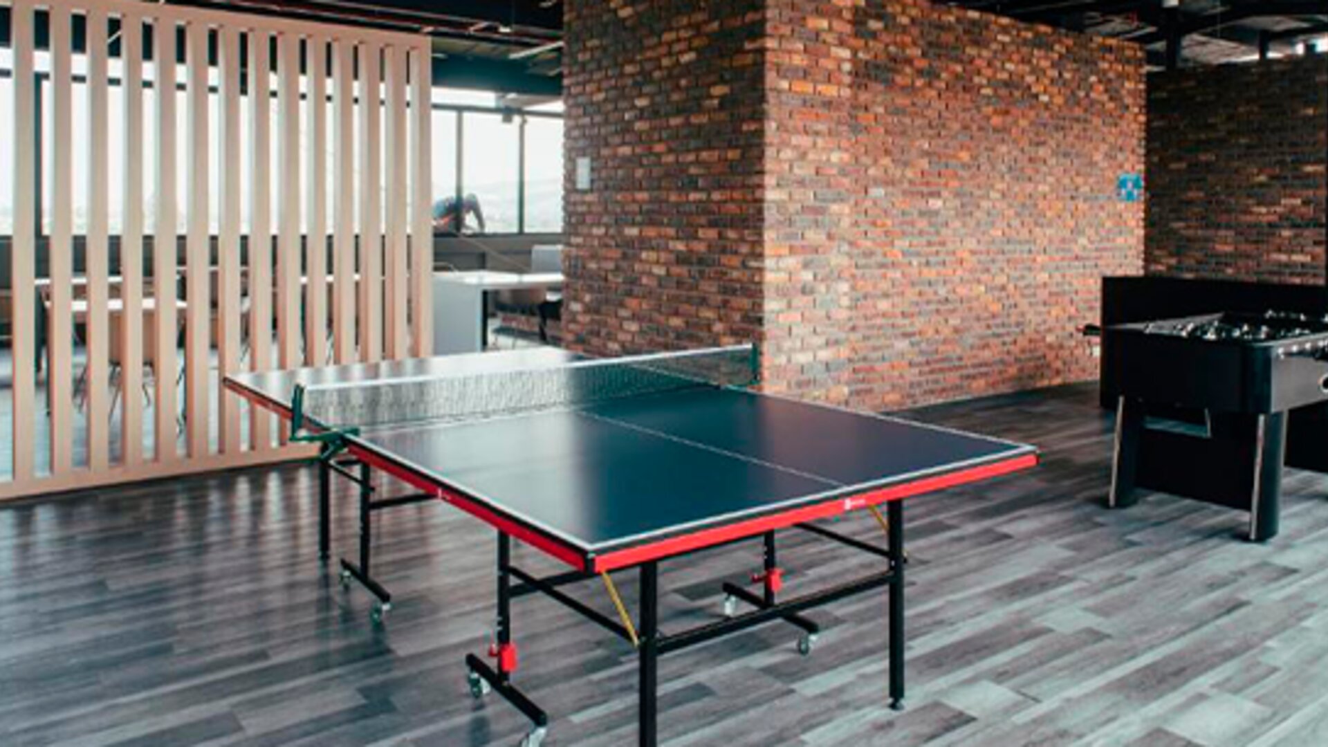 Recreation area with a table tennis table, foosball table, wooden slat partition and exposed brick walls at UMA Suites Chía.