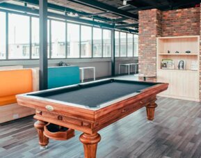 Games room with a wooden pool table, colourful booth seating, large windows and exposed brickwork at UMA Suites Chía.
