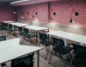 Communal study area with white tables, black chairs, exposed brick walls and wall-mounted lamps at UMA Suites Chía.