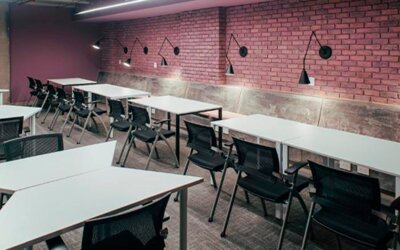 Communal study area with white tables, black chairs, exposed brick walls and wall-mounted lamps at UMA Suites Chía.