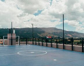 Rooftop sports court with blue flooring, basketball markings, safety netting and mountain views at UMA Suites Chía.