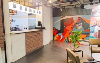 Reception counter with a brick-front desk, illuminated BRANDON lettering, colourful mural artwork, and indoor plants at Hotel Living 35 Suites.