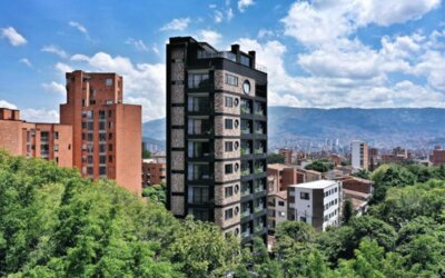 Exterior view of a multi-storey dark-brick hotel building surrounded by green trees, with city buildings and mountains in the background at Hotel Living 35 Suites.