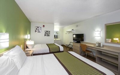 Guest room with two double beds, white bedding, green patterned runners, bedside lighting, a television, and a long desk with a mirror at American Inn Carlisle.