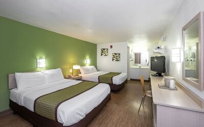 Guest room with two double beds, white bedding, green accent wall, matching bed runners, a television, and a long work desk at American Inn Carlisle.