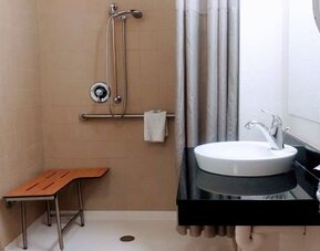 Bathroom with a walk-in shower, grab bars, shower seat, white vessel sink, black countertop, and folded towels at American Inn Carlisle.