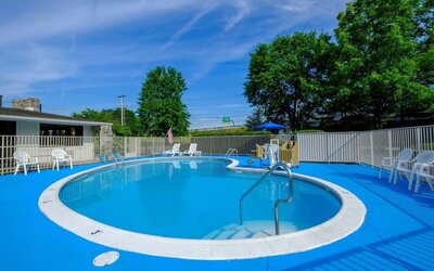 Outdoor swimming pool surrounded by a bright blue deck, white fencing, lounge chairs, and trees at American Inn Carlisle.