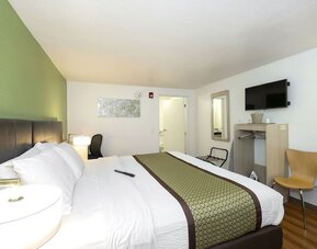 Guest room with a king-size bed, white bedding, green accent wall, bedside lamp, television, and compact work area at American Inn Carlisle.