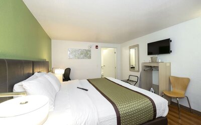 Guest room with a king-size bed, white bedding, green accent wall, bedside lamp, television, and compact work area at American Inn Carlisle.