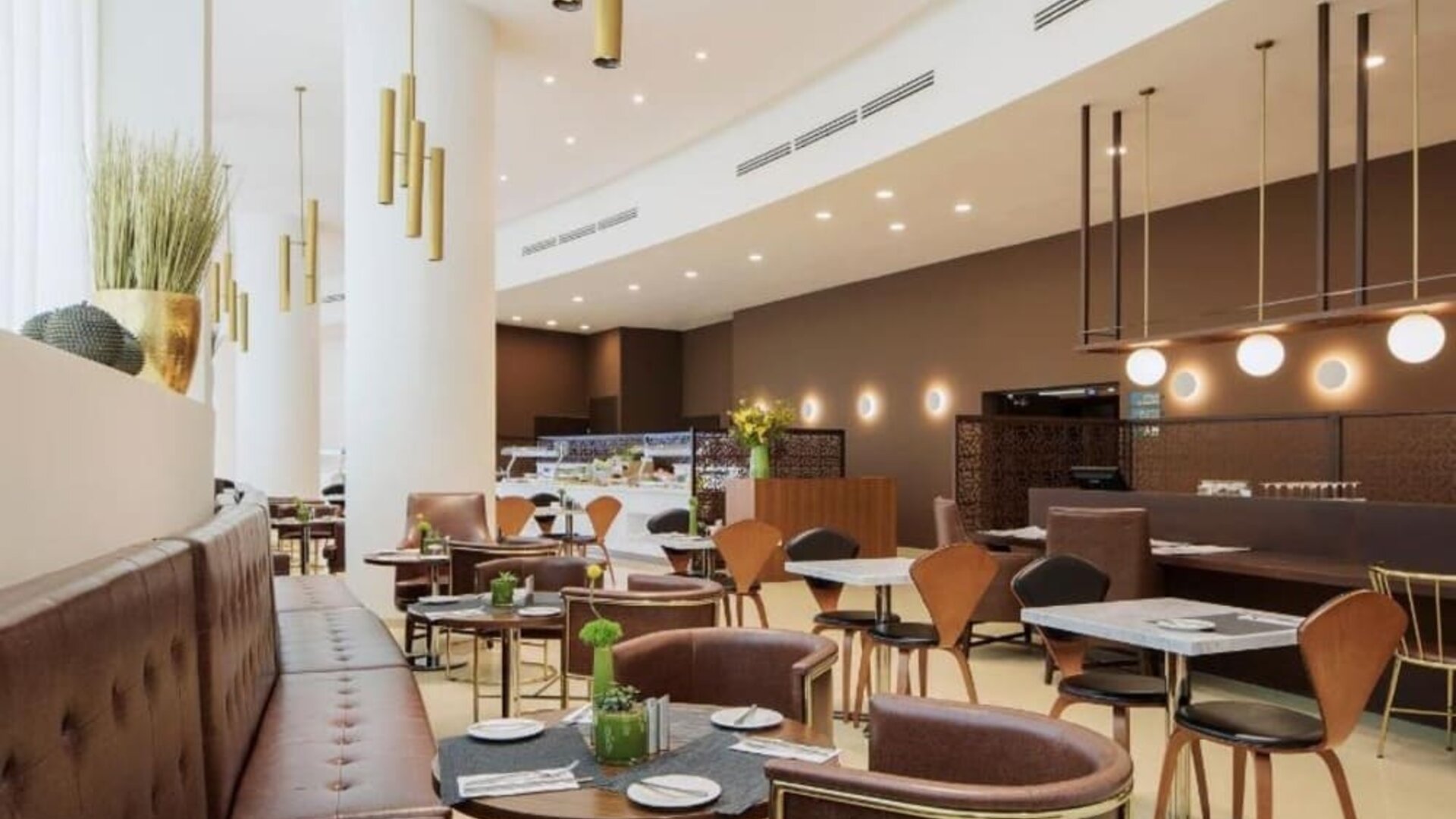Hotel restaurant and dining area featuring brown upholstered seating, wooden chairs, round tables, decorative pendant lights, and a buffet counter at Prima Millennium.