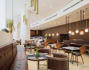 Hotel restaurant and dining area featuring brown upholstered seating, wooden chairs, round tables, decorative pendant lights, and a buffet counter at Prima Millennium.
