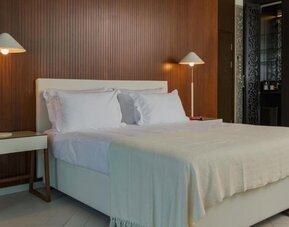 King bedroom featuring white bedding, a wood-panelled feature wall, bedside tables, matching lamps, and dark built-in wardrobes at Prima Millennium.